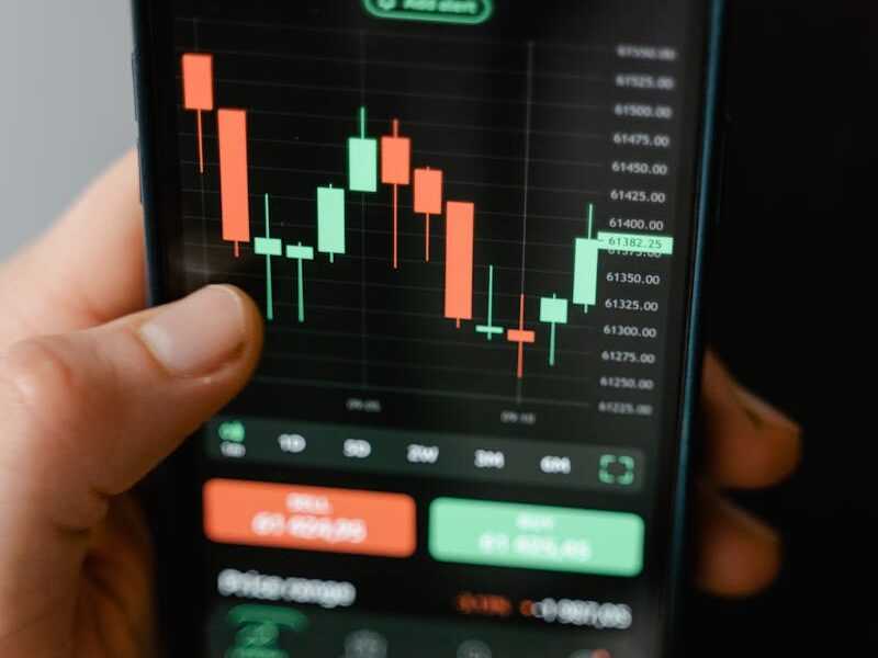 Hand holding smartphone displaying cryptocurrency trading graph in app.