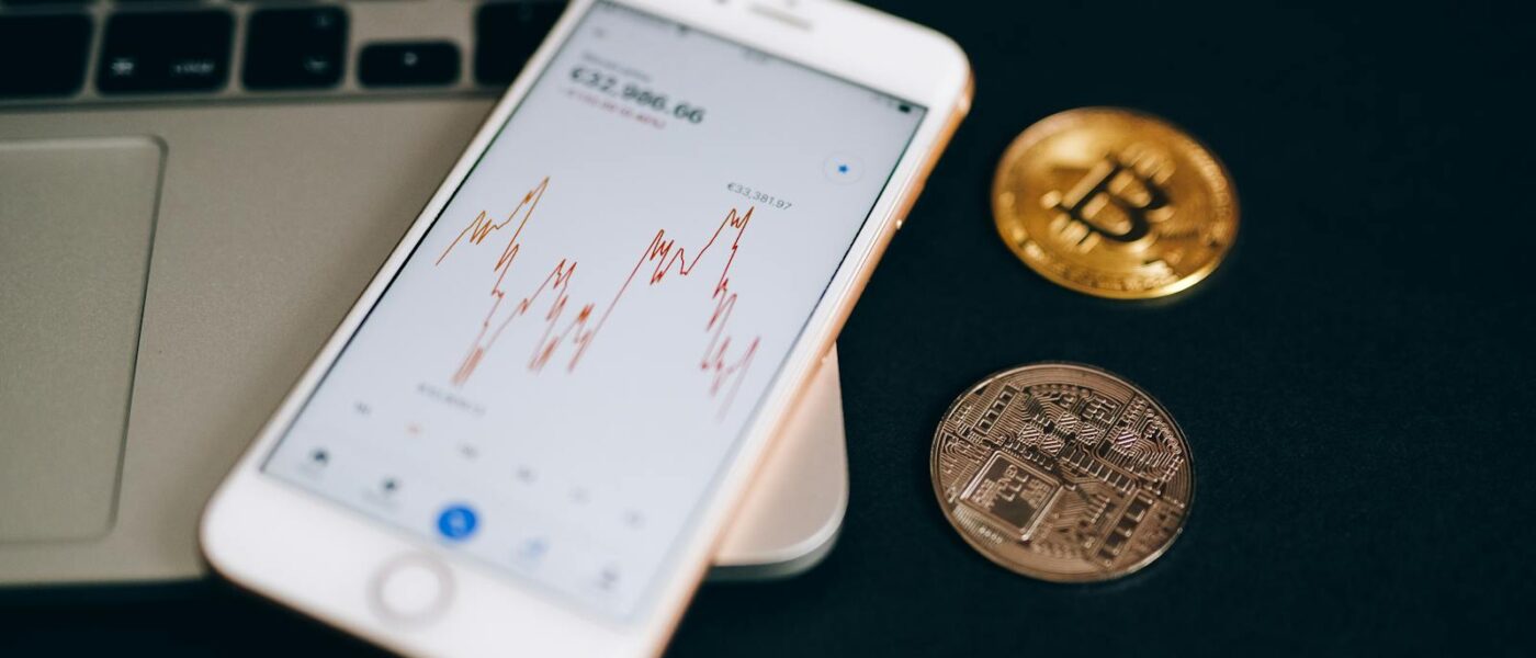 Close-up view of cryptocurrency coins and stock market graph on a smartphone screen.