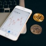 Close-up view of cryptocurrency coins and stock market graph on a smartphone screen.
