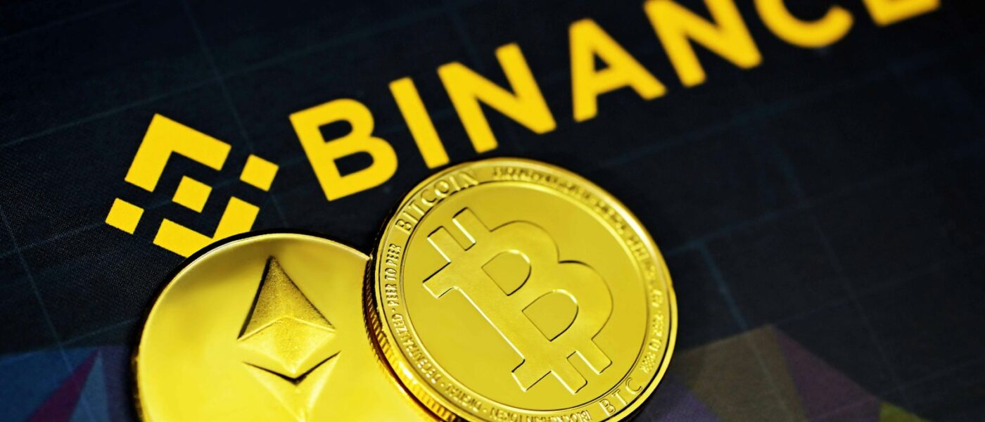 two gold bitcoins sitting next to a binance sign