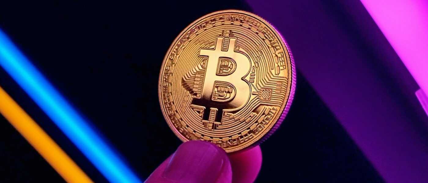 a hand holding a bit coin in front of a neon background