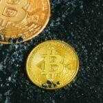 two gold bitcoins sitting on a black surface
