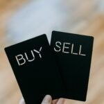 a hand holding two black cards with the words buy and sell written on them